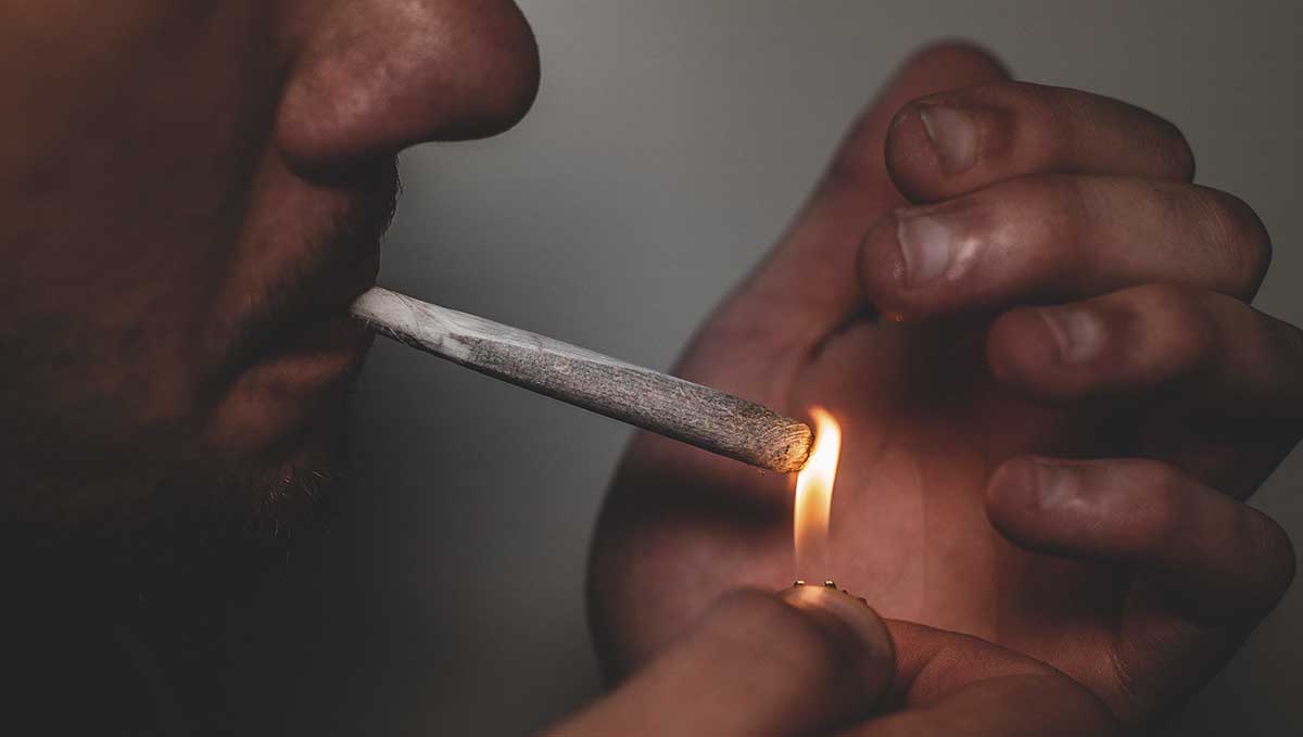 Spliff Definition &ndash; What Is a Spliff? A closeup of a man's face as he lights up a cannabis cigarette