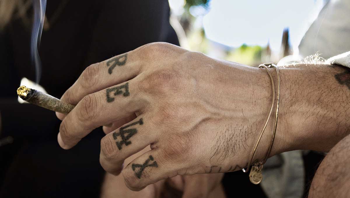Spliff Definition &ndash; What Is a Spliff? A man's hand with a RELAX tattoo on the fingers holding a joint