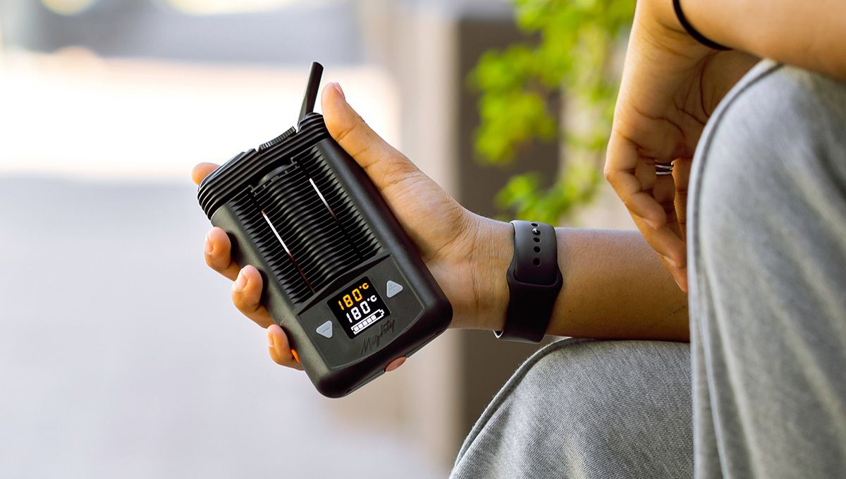 Tips For Choosing Best Plants Pens To Puff In: A closeup of young man's hands holding a big portable vaporizer with temperature settings