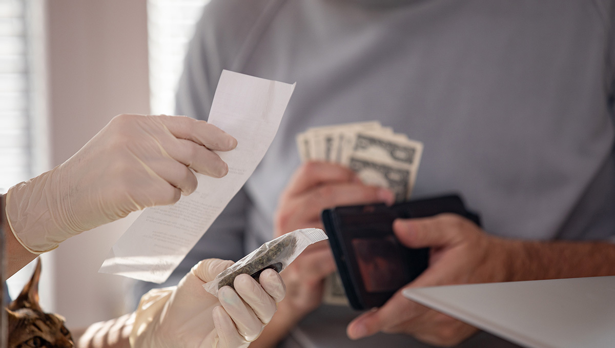 Two persons' hands as they exchange weed for cash in what seems like a legal dispensary