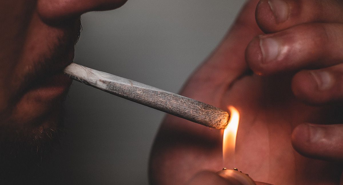 A closeup of a man's face and hands as he lights up a joint