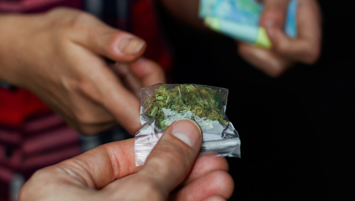 Hvor Meget Er Et Halvt Ounce Hash? Den Komplette Prisguide: Et closeup af to personers hænder, der udveksler penge og en ziplock-pose med cirka ét gram cannabis